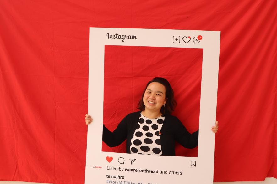 Photo from 2022 World Aids Day celebrations in Tasmania, featuring a woman posting in front of a red background