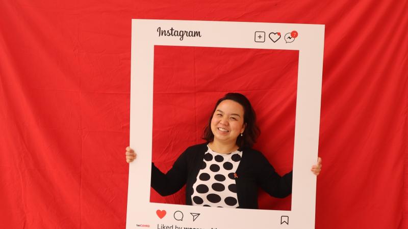 Photo from 2022 World Aids Day celebrations in Tasmania, featuring a woman posting in front of a red background